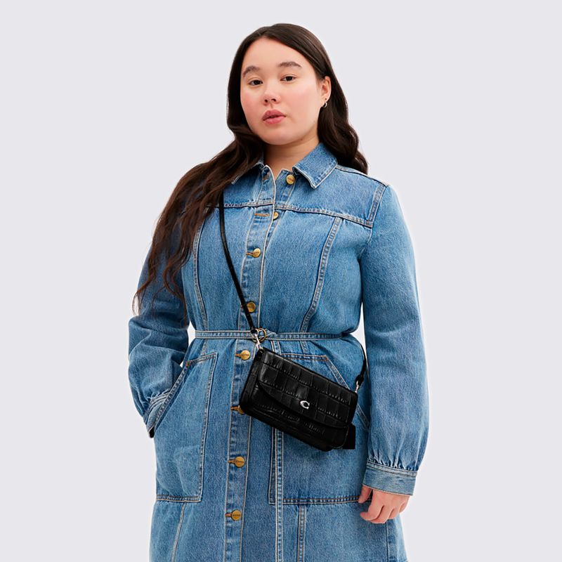 mulher com sobretudo jeans e bolsa pequena de lado coach preta